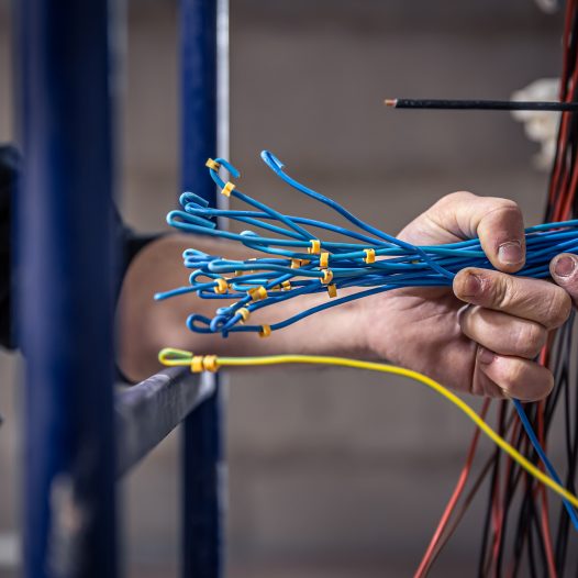 A construction electrician cuts a voltage cable during a repair, close up.